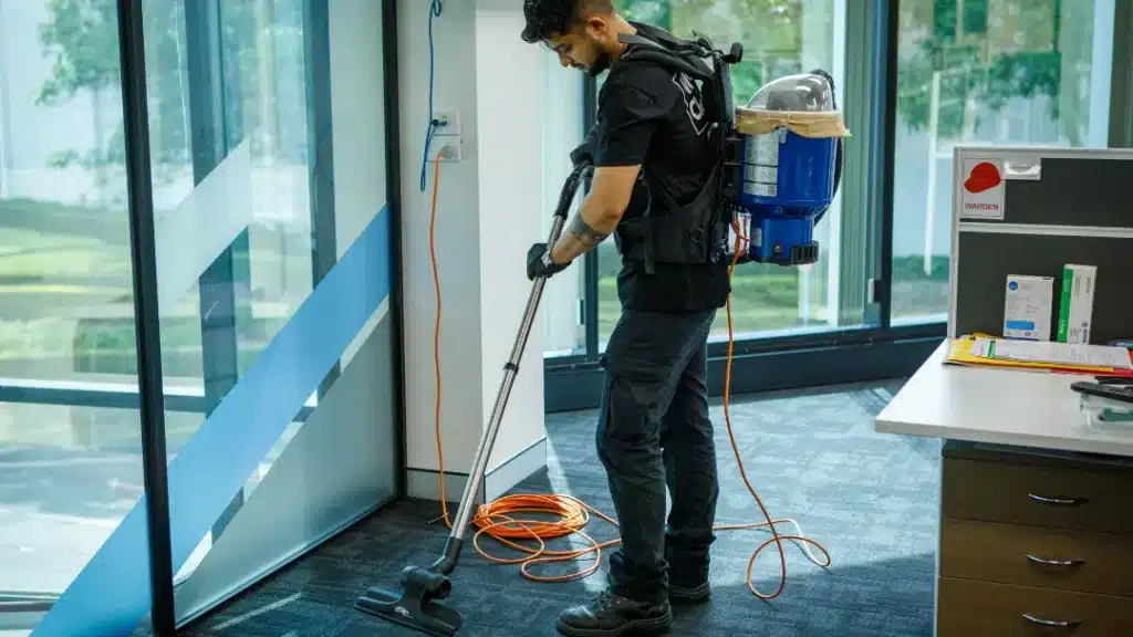 Professional cleaner using backpack vacuum on office carpet in modern Sydney commercial space